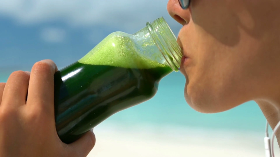 young woman drinking green vegetable smoothie on beach closeup of female enjoying summer vacation she is living healthy lifestyle outdoors smiling bavvmqjfe thumbnail full04
