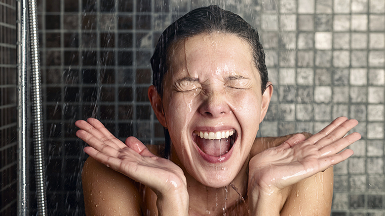 Young woman reacting in shock to hot or cold shower water as she stands under the shower head washing her hair eyes closed with her hands raised and mouth open; Shutterstock ID 245687524; PO: cold-shower-wake-up-stock-TODAY-tz-150422; Client: TODAY digital