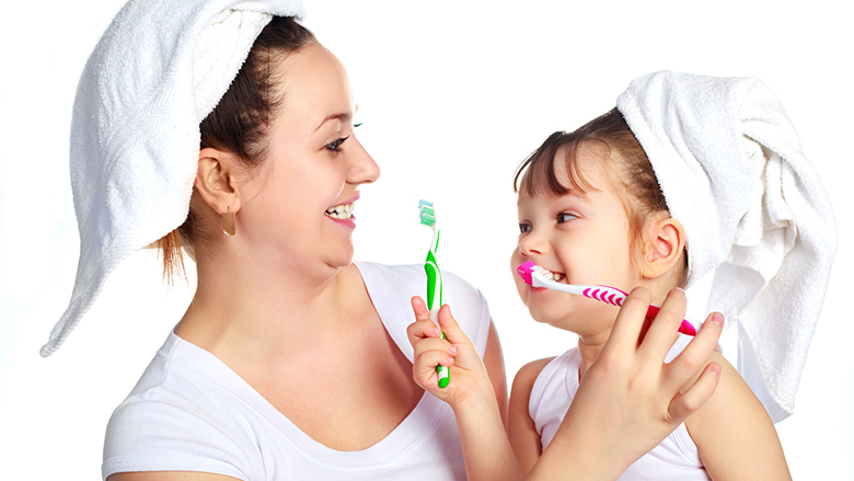 Young beautiful mother and her little daughter brushing teeth and laughing