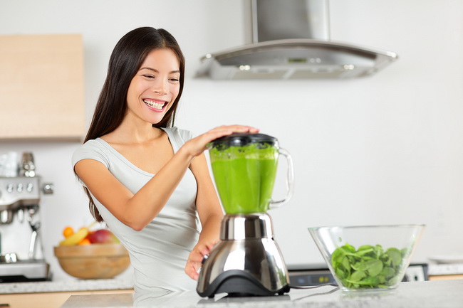 Vegetable smoothie woman blending green smoothies with blender home in kitchen. Healthy eating lifestyle concept portrait of beautiful young woman preparing drink with spinach, carrots, celery etc.