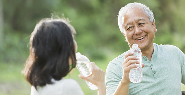 Senior Asian couple (60s) talking, drinking water outdoors