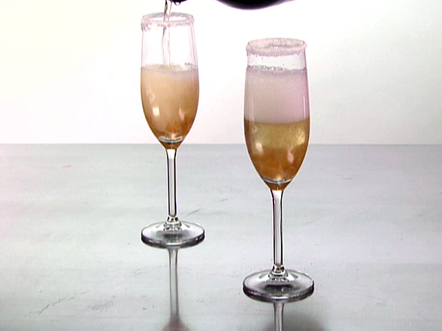 A unique and different drink is being poured into two glasses. These glasses hold a champagne cocktail that is good for you and contains an infusion of ginger and candied ginger.