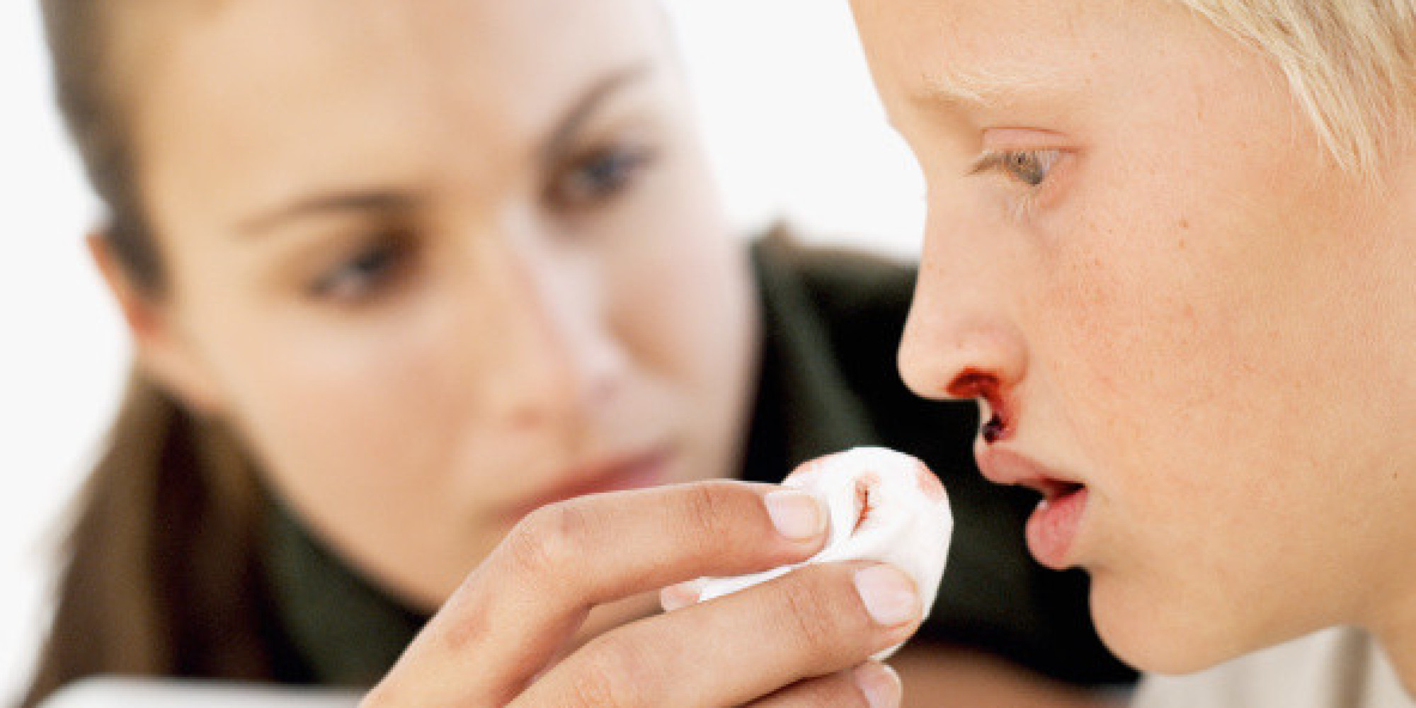 Young woman cleaning the bleeding nose of young boy (8-10) with cotton wool