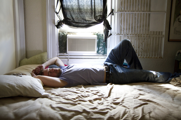 A man reclining on a unmade bed.