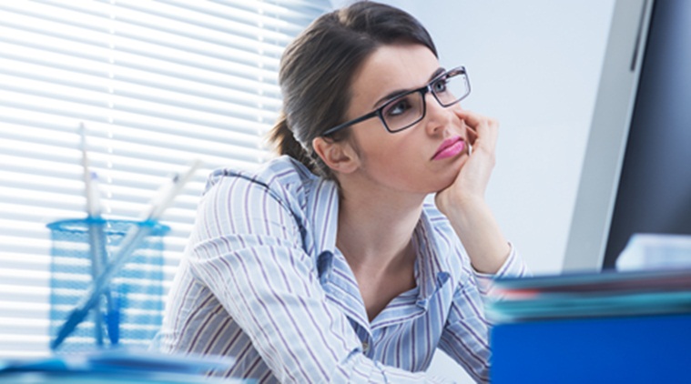 Bored office worker at desk staring at computer screen with hand on chin.