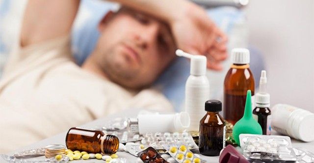 man-with-hand-over-his-head-feeling-ill-in-background-with-close-view-of-pills-and-medicine