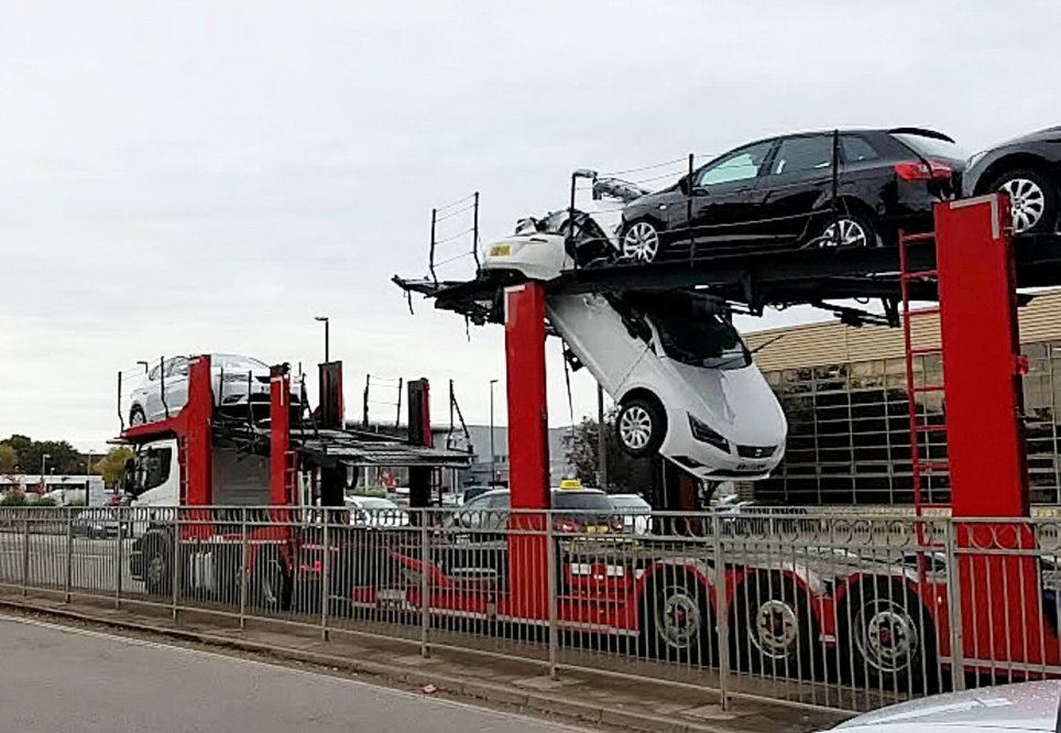 This is the scene of devastation after a vehicle transporter smashed into a bridge while stacked with pristine cars - tearing one in HALF. See SWNS story SWCAR. Dramatic photos show the front of a crushed white Seat hanging through the middle layer of the lorry while the rear end is left behind. The new car, thought to have a 2015 plate, was destroyed when the driver of the transporter misjudged the height of a new pedestrian footbridge. Office workers said they heard an "almighty crash" when cars on the top level collided with the bridge. Support engineer Richard Pithouse jumped up from his desk when he heard the commotion, on Gatwick Road, Crawley, at 10.30am on Friday.