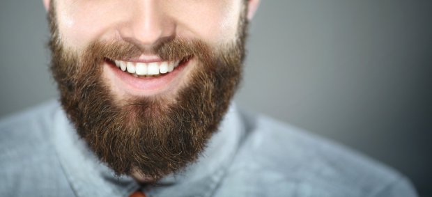 Closeup portrait of smiling unrecognizable bearde man. He's facing the camera and smiling with perfect set of teeth. Wearing light blue smart casual shirt. Shot oer gray background.