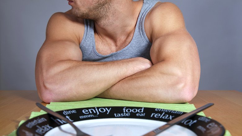 Muscular man sitting at the table with empty plate