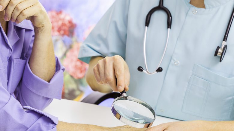 Dermatologist looking at woman's hand through a magnifying glass