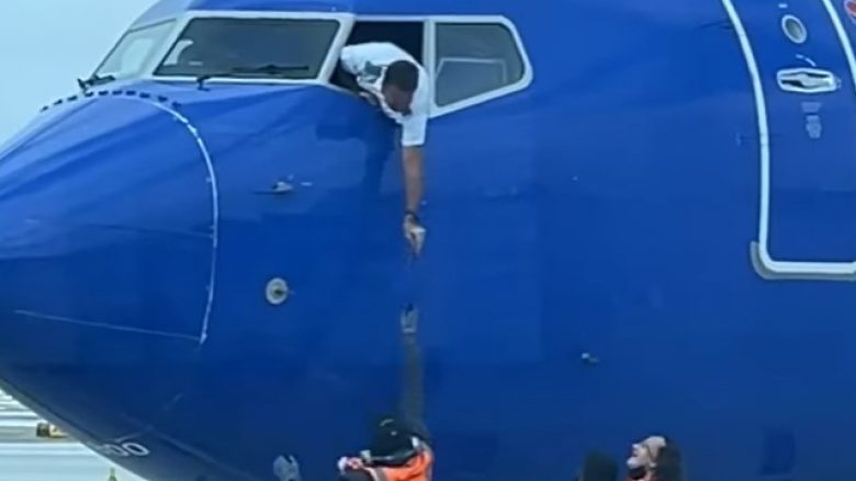 Piloti varet nga dritarja e kabinës së aeroplanit për marrë telefonin e humbur të pasagjerit