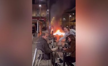 Protestat në Francë, një çift shijon një gotë verë teksa një zjarr shihet në prapavijë