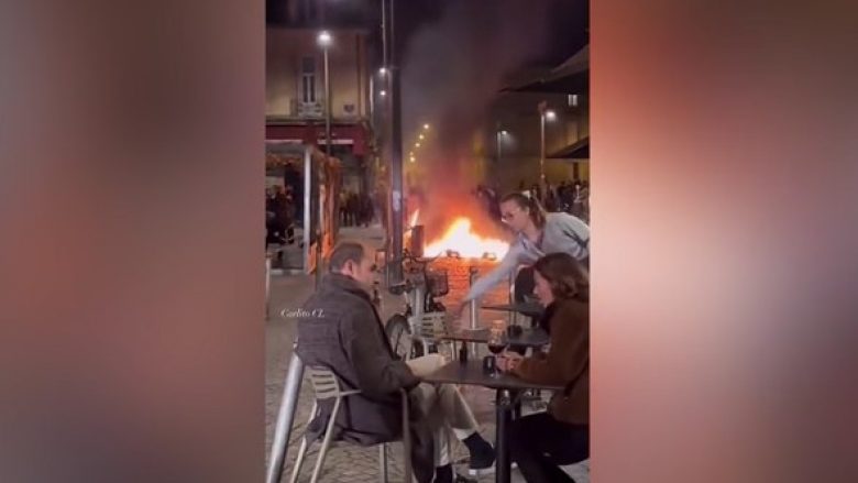 Protestat në Francë, një çift shijon një gotë verë teksa një zjarr shihet në prapavijë